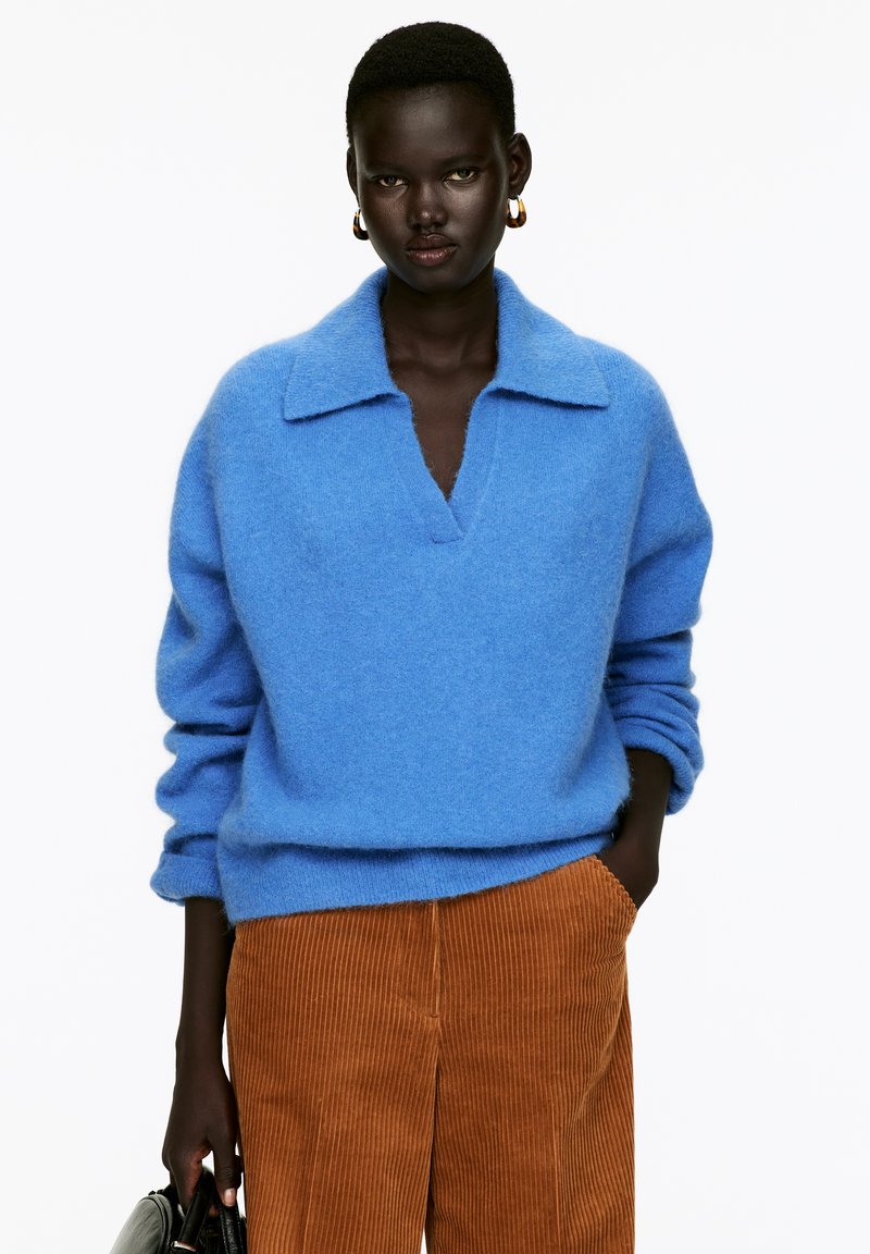 Hellblaues Wollpullover mit Kragen und V-Ausschnitt, kombiniert mit braunen Cordhosen mit gerippter Textur und geradem Bein.