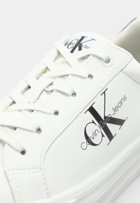 Valge nahast tennisekingad, millel on nööpide sulgemine, logo detail "Calvin Klein Jeans", sile tekstuur ja ümar varvaste disain.