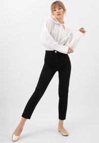 Chemise blanche à boutons avec manches longues, rentrée dans un pantalon noir taille haute, associé à des ballerines dorées. Design simple et épuré.
