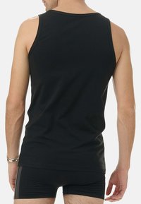 Svart bomullstopp med en figurnära design, breda ärmhål och en slät textur, bäres över mörka shorts. Bakifrån framhäver enkelhet.