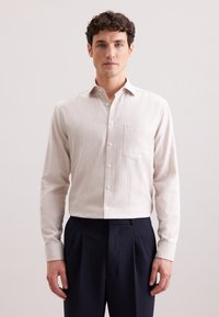 Jasnobeżowa koszula zapinana na guziki, wykonana z teksturowanej tkaniny, z kieszenią na klatce piersiowej i klasycznym kołnierzykiem, zestawiona z granatowymi spodniami.