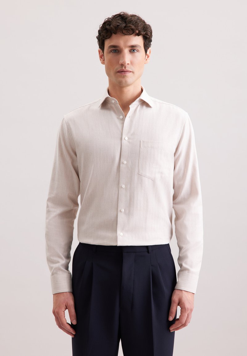 Jasnobeżowa koszula zapinana na guziki, wykonana z teksturowanej tkaniny, z kieszenią na klatce piersiowej i klasycznym kołnierzykiem, zestawiona z granatowymi spodniami.