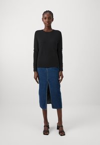Zwarte gebreide top met lange mouwen gecombineerd met een blauwe denim midi-rok met een split aan de voorkant, aangevuld met zwarte blokhak-sandalen.