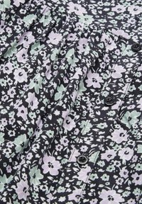 Schwarzer Stoff mit einem floralen Muster, das kleine rosa und grüne Blumen zeigt. Gerafftes Design mit sichtbaren schwarzen Knöpfen entlang der Mitte.