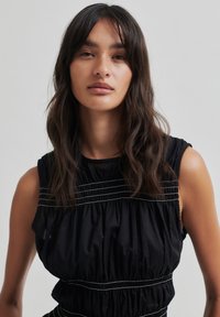 Juoda be rankovių suknelė su susiraukšlėjusiu audiniu, turinti horizontalius siuvimo raštus per liemenį. Lygi tekstūra, laisvas siluetas.