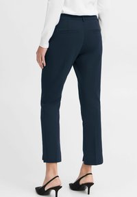 Námořnické kalhoty na míru s elegantním designem, bočními kapsami a zkrácenou délkou, spárované s černými sandály na podpatku. Hladká textura tkaniny.