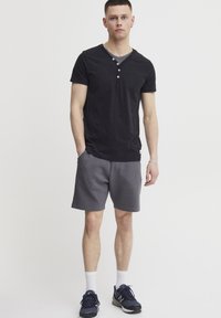 Black cotton short-sleeved t-shirt with V-neck and three-button placket paired with gray textured shorts. Worn with navy athletic shoes.