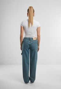 Blugi bleu deschis cu talie înaltă și croială lejeră, cu buzunare în stil cargo și o pată de piele pe partea din spate a taliei.