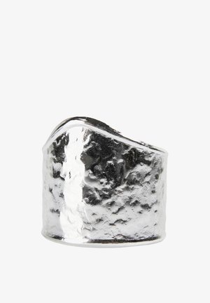 Anillo ancho de plata con textura martillada y un borde superior asimétrico y angulado sobre un fondo blanco.