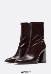 Bordové kožené kotníkové boty z umělé kůže s špičatou špičkou, zipovým uzavřením a masivním podpatkem. Lesklý povrch se jemnými švy.