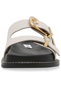Beige slipper sandalen met brede banden, gouden accenten en een zwarte zool. Voorzien van uitsparingen en contrasterend stiksel langs de randen.