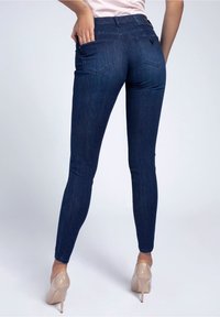 Jeans skinny de denim azul oscuro con una cinturilla alta, dos bolsillos traseros y una textura suave. Combinados con tacones altos nude.