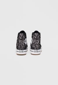 Melna un rozā zebra raksta augstpapēžu sporta apavi ar baltu vidusdaļu un brūnu gumijas zoli; īpašības iekļauj ikonisko Converse zvaigžņu logo sānos.