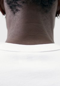 Weißes Baumwoll-T-Shirt mit Rundhalsausschnitt, glatter Textur und kurzen Ärmeln. Verfügt über eine sichtbare Naht am Kragen und dezente Nähdetails.