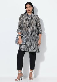 Tunic a righe bianche e nere con colletto, abbinata a pantaloni neri e sandali con tacco bianchi. Accessoriata con una borsa luccicante.