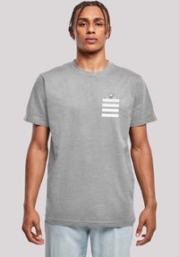Pilkos medvilninės T-shirt marškiniai su krūtinės kišene su spaudiniu, trumpomis rankovėmis ir apvalia apykakle. Modelis dėvi šviesiai mėlynas džinsus.
