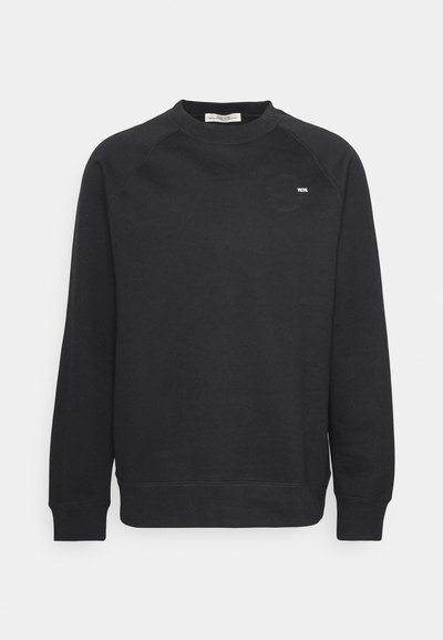 Sweatshirt noir en tissu doux, avec un col rond, des manches raglan longues, des poignets côtelés, et un petit logo sur la poitrine.