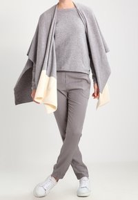 Una sciarpa grigia in lana sopra un maglione grigio chiaro, abbinata a pantaloni grigi chiari e scarpe da ginnastica bianche. La sciarpa presenta una finitura color crema.