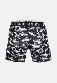 Boxer neri con motivo grafico di squali bianchi. Presentano un ampio elastico con la scritta "SEASIDE" in colori a contrasto.