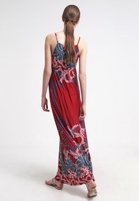 Robe maxi rouge avec motifs floraux bleus, bretelles spaghetti et tissu fluide. Texture lisse et coupe longue, idéale pour un look décontracté.