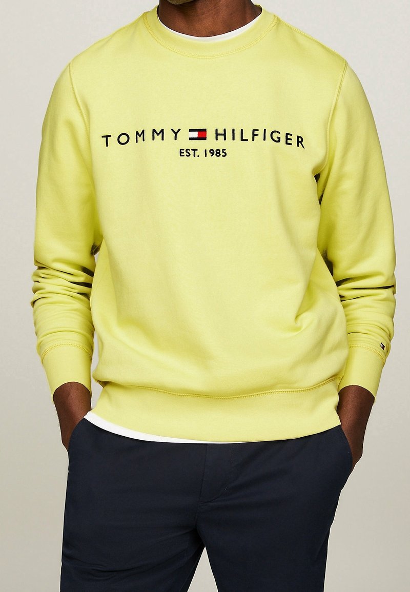 Světlounce žlutá mikina s kulatým výstřihem, s logem "TOMMY HILFIGER EST. 1985" vyšitým černou a červenou nití. Žebrované manžety a lemy.