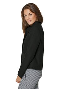 Zwarte op maat gemaakte blazer met een gestructureerde kraag, vervaardigd uit een textuurstof. Model draagt een getailleerde geruite broek en toont een zijprofiel.