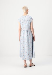 Μάξι φόρεμα σε ανοιχτό μπλε ύφασμα με λουλουδάτο σχέδιο. Διαθέτει κοντά μανίκια, πτυχώσεις στην πλάτη και ροή στη σιλουέτα. Φοριέται με επίπεδες παντόφλες.