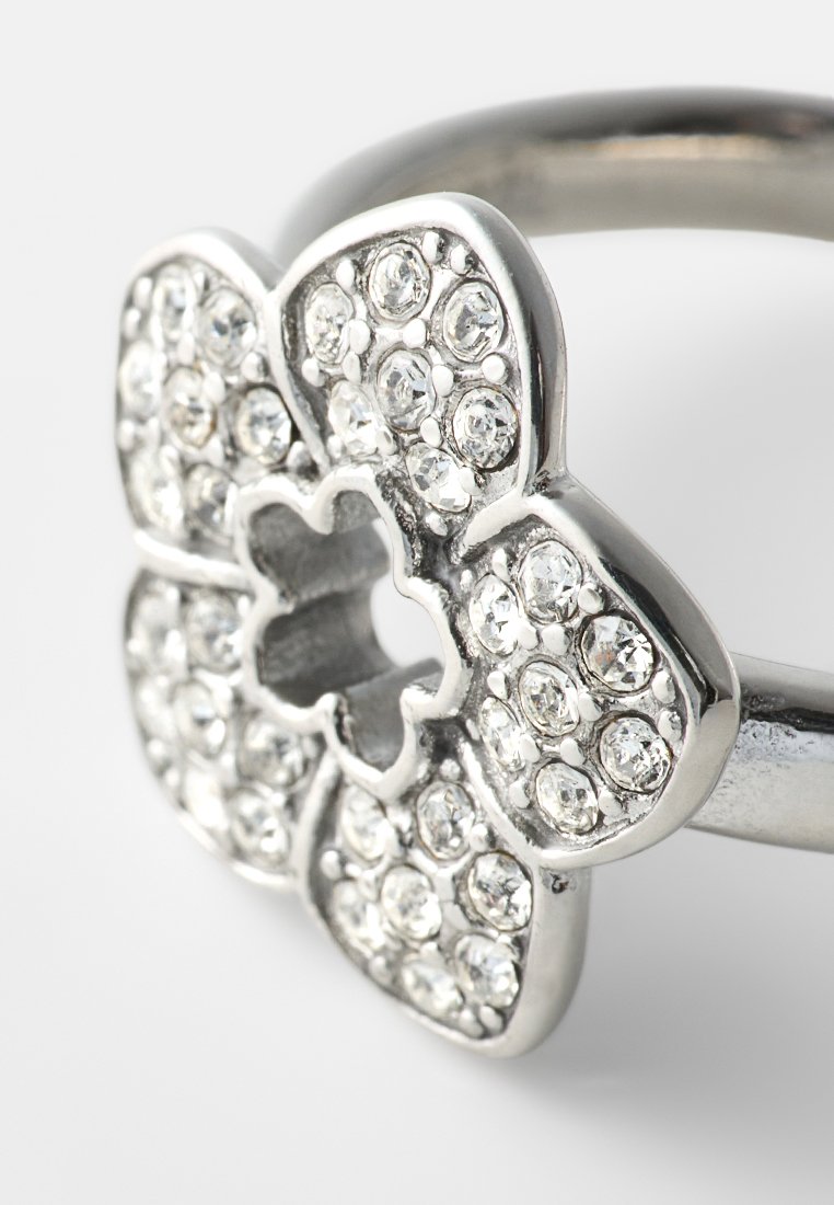 Anillo plateado con forma de flor, con gemas redondas y claras incrustadas en cada pétalo y un recorte en forma de trébol en el centro.