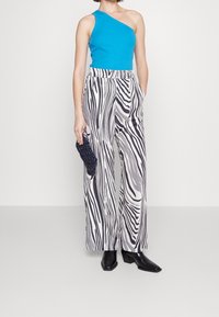 Niebieski top na jedno ramię, szerokie spodnie w pasy zebry w czarno-białym kolorze, o fakturowanej tkaninie, w zestawieniu z czarną kopertówką i butami z ostrym noskiem.