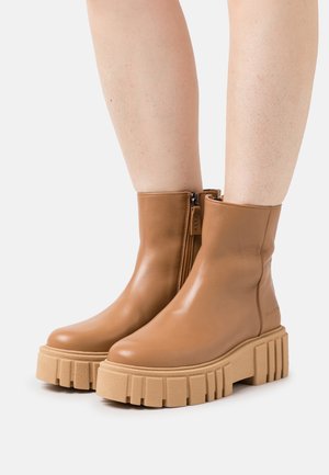 Braune Leder-Stiefeletten mit einem seitlichen Reißverschluss und einer dicken beigen Plateausohle mit gerippter Oberfläche. Glatte Oberfläche, minimalistisches Design.