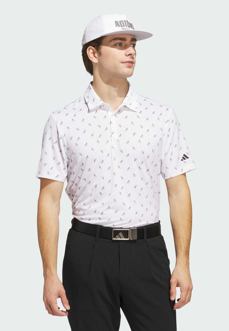 White polo shirt with a pattern of small black triangles, paired with black trousers and a white cap featuring the text "ADIDAS" in black.