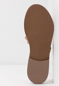 Sandal plat marron avec une semelle lisse, présentant un design de bride simple. La semelle intérieure affiche un logo en relief et la taille : 38.