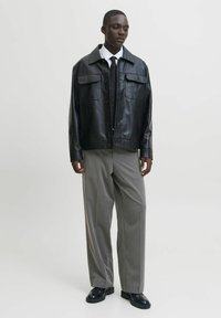 Black leather jacket with a collar and button closure, paired with gray pleated trousers and black shoes, creating a tailored look.