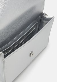 Sömskinnsaxelväska i silver med klaffstängning, utrustad med ett inre zipfack och en slät foder.