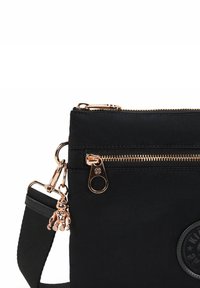 Svart nylon tvärsöverväska med guldfärgade detaljer, med dragkedjestängning, justerbar rem och en metallberlock i form av en nallebjörn.