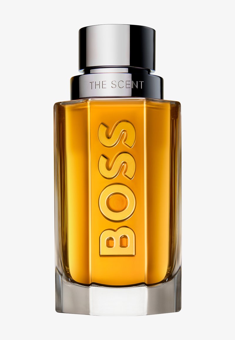 Transparente Glas-Parfümflasche mit bernsteinfarbener Flüssigkeit, silbernem Verschluss und dem auf der Vorderseite eingeprägten Schriftzug "BOSS THE SCENT".