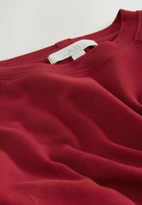 Piros pamut kerek nyakú pulóver, sima textúrával, látható varrási részletekkel és a "N.82" felirattal ellátott címkével.