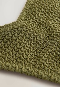 Olivgrön textil med en strukturerad, volangyta och växlande vågiga mönster. Det mjuka tyget ger en något elastisk känsla.
