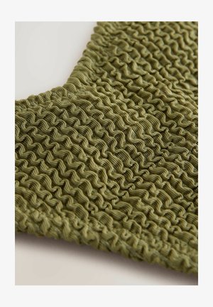 Oliivivihreä kangas, jossa on teksturoitu, rypistyksellinen pinta, jossa on vuorotellen aaltoilevia kuvioita. Pehmeä materiaali antaa hieman joustavan vaikutelman.