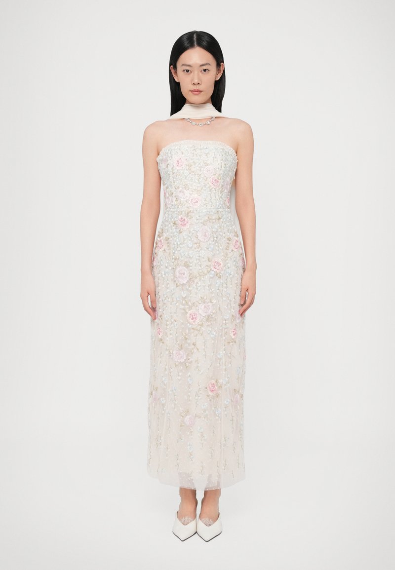 Suknia bez ramiączek z lekkiego, przezroczystego materiału, ozdobiona pastelowym haftem kwiatowym i cekinami. Kończy się w połowie łydki, zestawiona z białymi butami na obcasie.