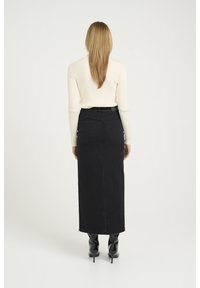 Gonna lunga in denim nero con taglio dritto, dotata di due tasche posteriori e vita alta, abbinata a un top a maniche lunghe a coste color crema.