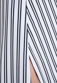White fabric with thin navy vertical stripes. Features a side slit for contrast. Smooth texture, modern design with a clean look.