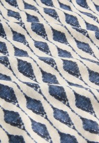 Tissu blanc avec un motif en losanges bleus, disposé de manière répétitive avec un léger effet ondulé et une surface texturée.