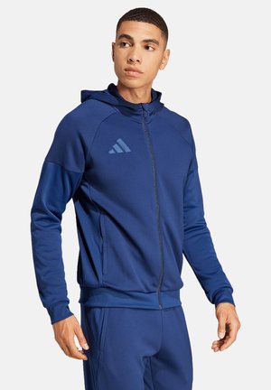 Navy-blaue Sport-Zip-Jacke mit Kapuze, aus glattem Stoff, mit diagonalen Nähten, Reißverschluss-Taschen und einem kleinen Logo auf der Brust.