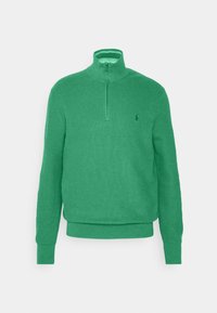 Grön, långärmad pullover i texturerat tyg med dragkedja vid kragen och en liten logotyp på vänstra bröstet.