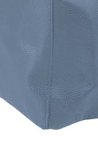 Coin d'un sac en cuir bleu clair avec une finition texturée, présentant des coutures visibles et une base légèrement arrondie.