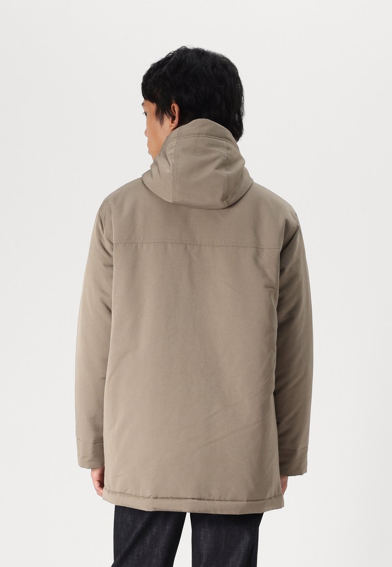 Beżowa ocieplana kurtka z kapturem. Posiada gładką teksturę, luźny krój i prosty design. Dolna część sięga do połowy uda.