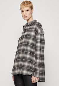 Camicia a quadri bianca e nera realizzata in tessuto, con bottoni, colletto e taglio dritto. Maniche lunghe con dettagli sottili.