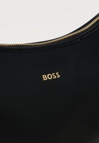 Fekete bőrfelület arany cipzárral és rajta kis arany betűk, amelyek a "BOSS" szót formálják.