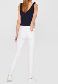 Marinefarbener ärmelloser Oberteil mit Schulterbändern, kombiniert mit weißen Slim-Fit-Jeans. Der Stoff ist glatt; die Jeans haben Gesäßtaschen und Schlitze an den Knöcheln.